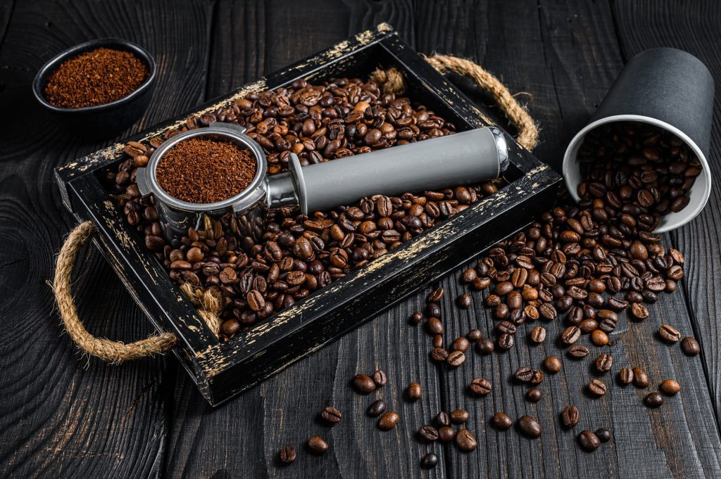 Ground Coffee in Portafilter for Espresso in a wooden tray with coffee beans.